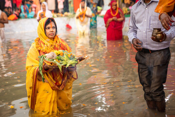 Women performing Chhath festival, standing in river water with offering prasad for God in their...