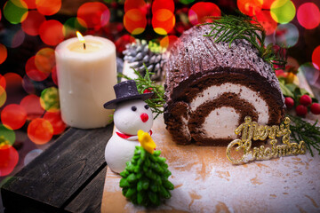 Fototapeta na wymiar Chocolate yule log cake with snowman and santa clause made from sugar on wooden table for celebrate in christmas and new year festival.