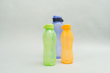 Plastic Bottles, eco bottles. A stack of colour water bottles, blue, orange and green, gathered on the right side, on a grey background.