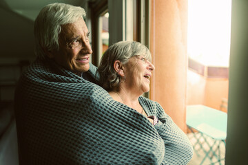 Elderly couple standing at home in front of the window and watching outside
