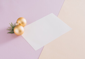 Christmas decoration idea, golden baubles, green fir and white paper card on pastel purple and beige background. Minimal seasonal copy space idea, creative aesthetic concept.