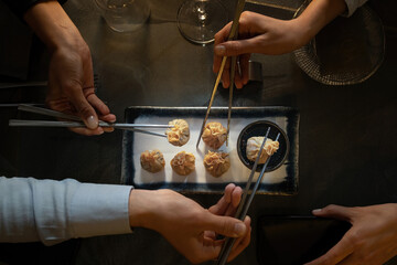 Closeup on dim sum, Chinese food disposed on a plate with group of friends hands holding chopstick.