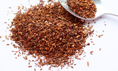 Rooibos tea in spoon, on white background, on table. Aspalathus linearis. Loose tea, dry leaves. Close up, macro.