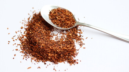 Rooibos tea in spoon, on white background, on table. Aspalathus linearis. Loose tea, dry leaves. Close up.