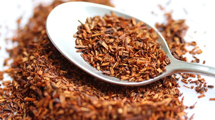 Rooibos tea in spoon, on white background, on table. Aspalathus linearis. Loose tea, dry leaves. Close up, macro.