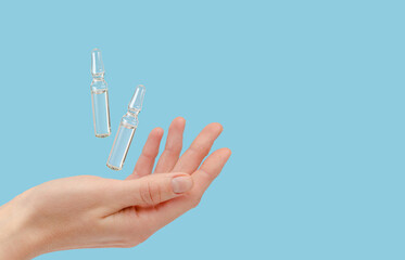 Ampoules flying over female hand on blue background. Copy space.