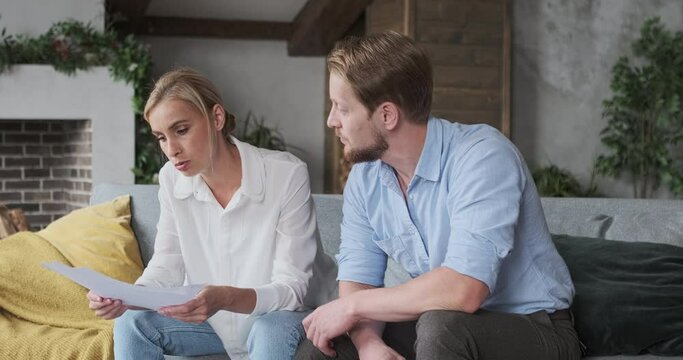 Angry wife scolding husband holding paper documents non payment bills mortgage checking bankruptcy credit at home. Family having financial conflict misunderstanding aggressive quarrel arguing dispute