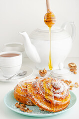 Homemade bakery. Pouring honey on sweet rolled bun with walnuts and grated coconut on white background. Breakfast table concept.