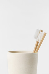 Fototapeta na wymiar Bamboo toothbrushes in eco cup on white background. Copy space, close up. Ecological materials concept.