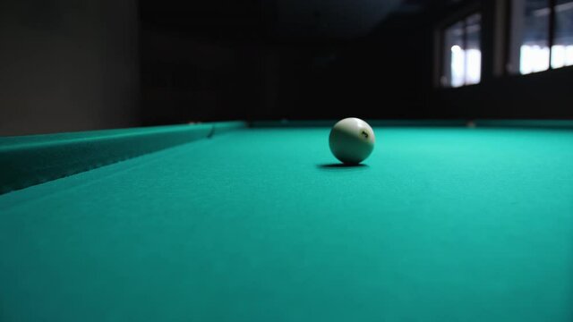 Lone billiard ball with the number three, slowly rolling across the green baize table in a dark gloomy room. Concept of games and entertainment.