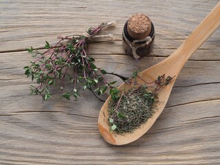 Dry herb in a wooden spoon and twigs of thymus grass, herbal tincture, oil on a wooden table, flat...