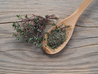 Dry herb in a wooden spoon and twigs of thymus grass on a light wooden table, flat layout....