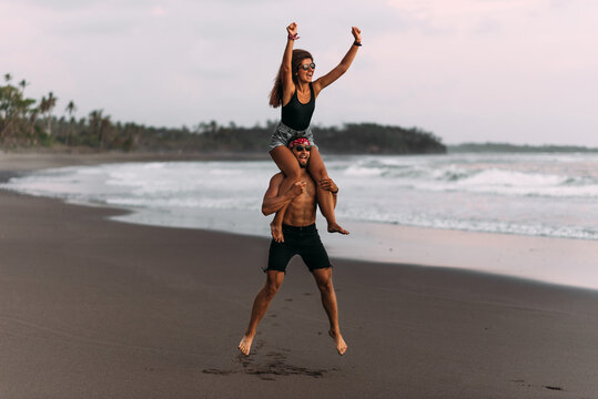 A happy couple is having fun on the seashore. A beautiful couple fooling around on the beach of the paradise island of Bali. The couple rejoices at the cancellation of the lockdown. Vacation at sea