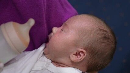 Cute little baby is hungry and opening its mouth ready to eat. Caring mother gives baby a bottle. Baby takes the milk bottle.