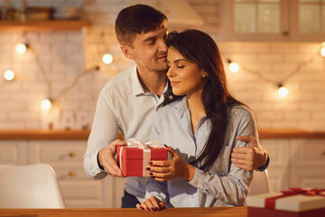 Love background. Man in love hugs and kisses his wife on the forehead, giving her a gift for Valentine's Day. Concept of congratulations on Valentine's Day, birthday, Christmas or Women's Day.