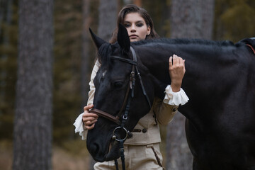 Naklejka premium Portrait of a rider in a retro suit and her black horse. A young brunette makes contact with a horse,