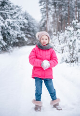 Fototapeta na wymiar Little girl in a bright jacket plays in the winter forest