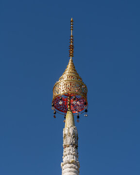 Bright golden hti or umbrella on top of ancient white stupa with blue sky background outside Wat Tham Chiang Dao cave buddhist temple, Chiang Dao, Chiang Mai, Thailand