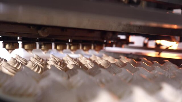 A number of freshly-made creamy marshmallows moving on the conveyor line. New marshmallows being squeezed at the backdrop. Close view.