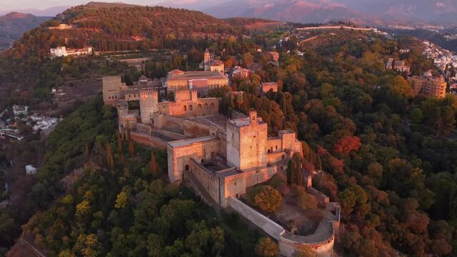 Dramatic aerial drone footage of the famous Alhambra palace and fortress in Granada, Andalusia, in Spain at sunset. Shot with a forward and tilt down motion. 