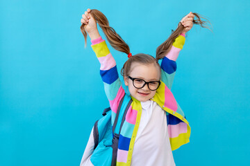 portrait of a cute little girl with glasses in a striped jacket with notebooks and a backpack...