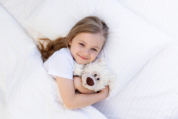 cute baby girl sleeping sweetly on the bed on a white cotton pillow under the blanket and smiling,...