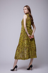 High fashion photo of a beautiful elegant young woman in a pretty robe-dress, white pants, brown top, shoes posing over white, soft gray background. Studio Shot. 