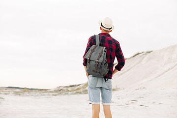 man traveler in a hat and with a backpack walks along a mountain road, man travel hiking in the Scandinavian mountains