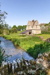 Fototapeta na wymiar The old stone dovecote (c.1600 AD) beside the infant River Windrush as it flows through the Cotswold village of Naunton, Gloucestershire UK