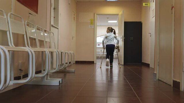St. Petersburg, Russia - October 11, 2021: Child walks along hospital corridor on crutches to see doctor. Girl has one leg broken in cast. High quality 4k footage