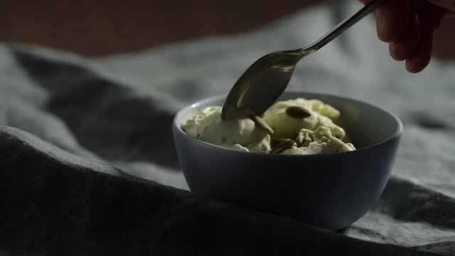 Slow motion eat pistachio ice cream in small blue bowl with pumpkin seeds
