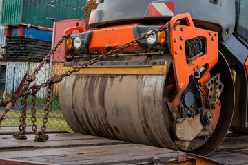 Details of an orange road roller standing on a transport trailer