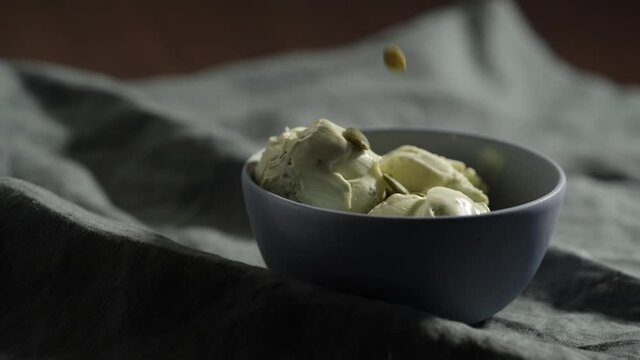 Slow motion decorating pistachio ice cream in small blue bowl with pumpkin seeds