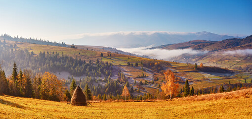 Mountain morning autumn panorama. Colorful fall landscape, foggy sunrise in Carpathians. Majestic misty scenery, valley, village