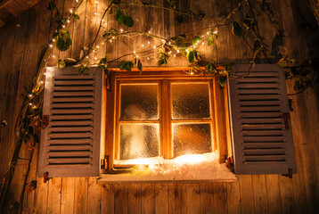 Weihnachtlich verschneites und beleuchtetes Fenster an einer Holzhütte
