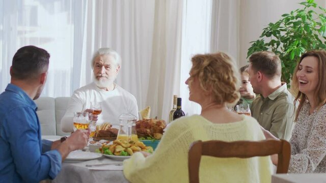 Waist up portrait view of the multi generation family sitting at the dining table during festive dinner, feeling happy, drinking wine and talking