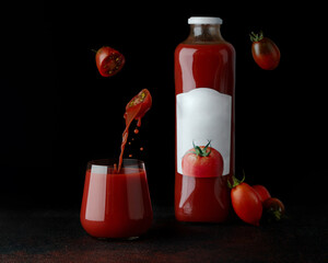 fresh tomatoes juice in glass on dark background and bottle of juice near. sliced two half tomatoes levitation. tomatoes juice pouring into glass.