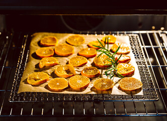 Orangenscheiben, Orangen in Scheiben geschnitten liegen zum trocknen auf einem Gitterrost auf Backpapier im Backofen. Daneben Rosmarin für ein gutes Aroma. geringe Schärfentiefe und selektive Schärfe.