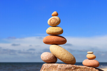 Rock zen pyramid of white and pink pebbles on a background of blue sky and sea.