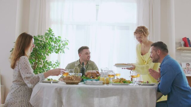 Festive table with different food and wine. Woman bringing fresh cooked pie with cream and putting at the table. Family dinner party friendship celebration