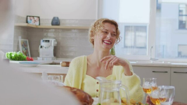 Happy family having dinner at the table. Blonde curly woman telling something emotionally and clinking with glasses with her relatives