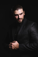 Business portrait of a white caucasian man in a black classic suit on a black background. Bearded man looks confident eyes.
