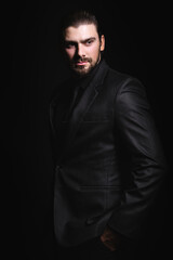 Naklejka premium Business portrait of a white caucasian man in a black classic suit on a black background. Bearded man looks confident eyes.