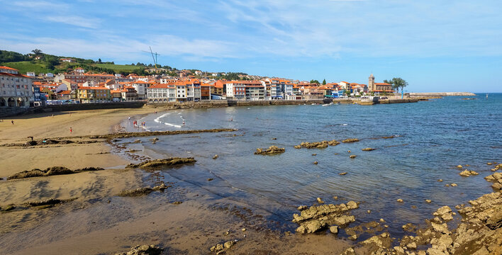 Village on the coast of the Cantabrian Sea. The church tower at one end and people bathing in the sea. Luanco Asturias. Spain