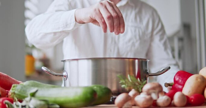 the chef adds spices and salt to the cooking dish in a metal saucepan.