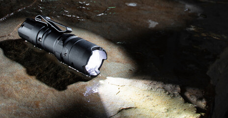 Waterproof flashlight on a wet rock - obrazy, fototapety, plakaty