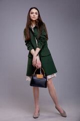 Fashion model in green coat with handbag, beautiful young woman. Studio shot. Gray background. 
