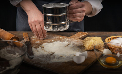Women's hands, flour and dough. A woman in an apron cooking dough for homemade baking, a rustic home cozy atmosphere, a dark background with unusual lighting.