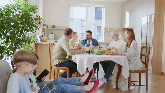 Company of caucasian family drinking wine glasses and chatting. Happy people laughing and talking in the summer evening while kids running nearby