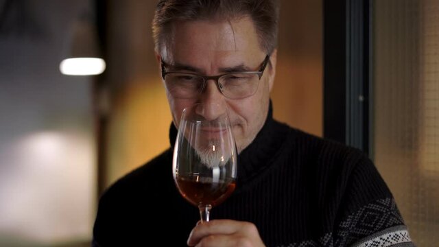 Man drinking wine at home. Winter, cosy warm room, pullover. Professional wine expert, sommelier holding glass of wine, tasting, rating and reviewing.